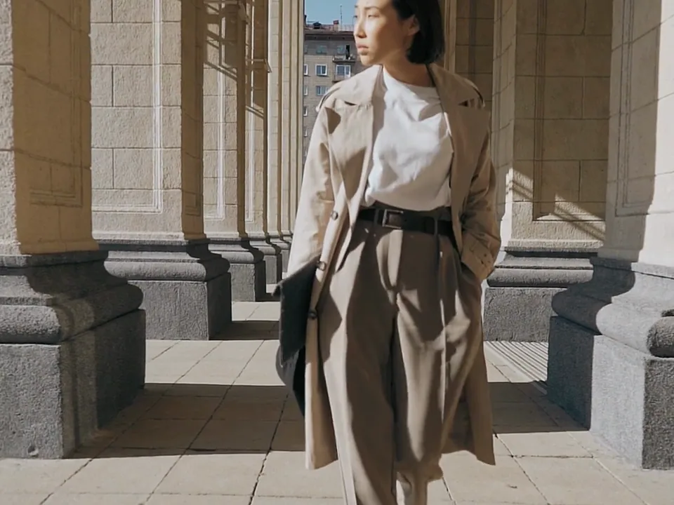 A woman in a trench coat walking under a colonnade