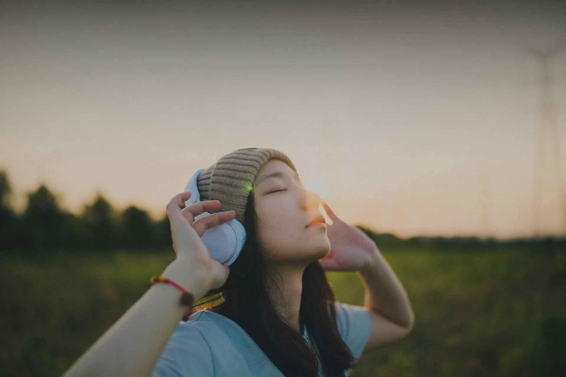 A woman with headphones listening at sunset