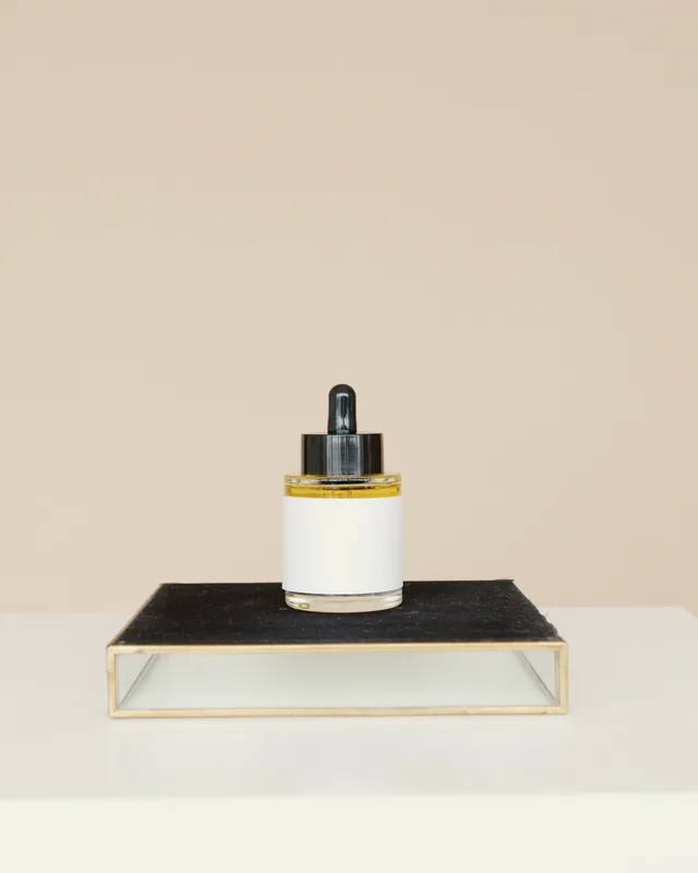 A serum bottle on a black plinth against beige