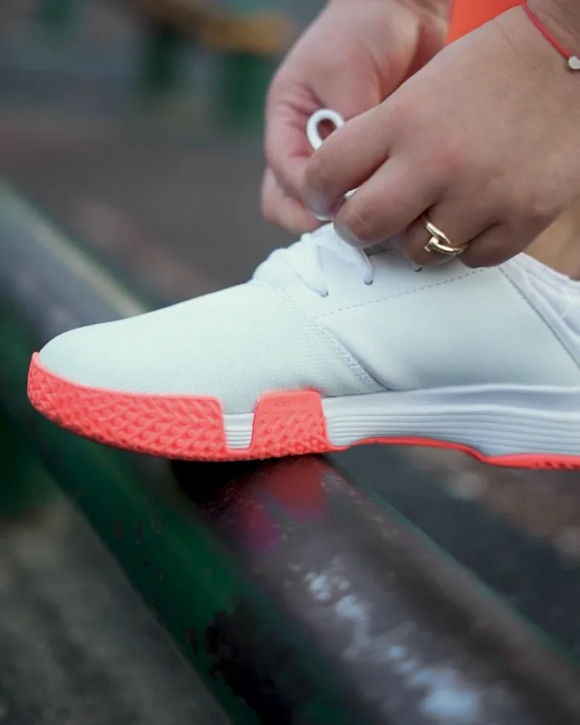 A runner tying a white and coral sneaker