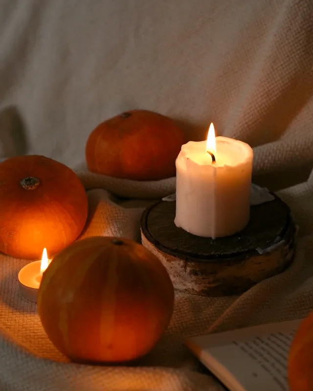 A white candle burning beside small pumpkins
