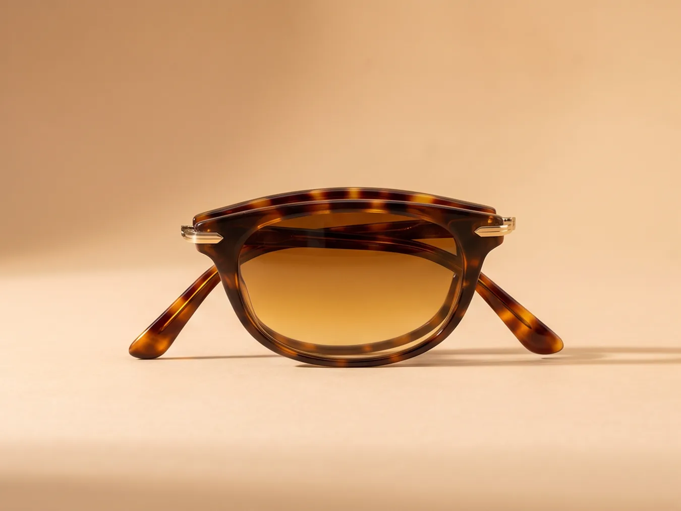 A pair of tortoiseshell sunglasses on a sand backdrop, from a new angle