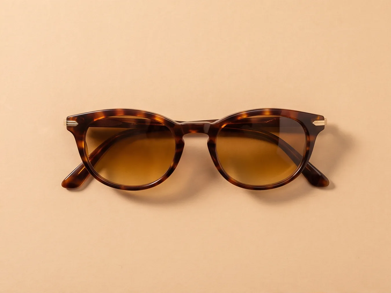 A pair of tortoiseshell sunglasses on a sand backdrop, from a new angle
