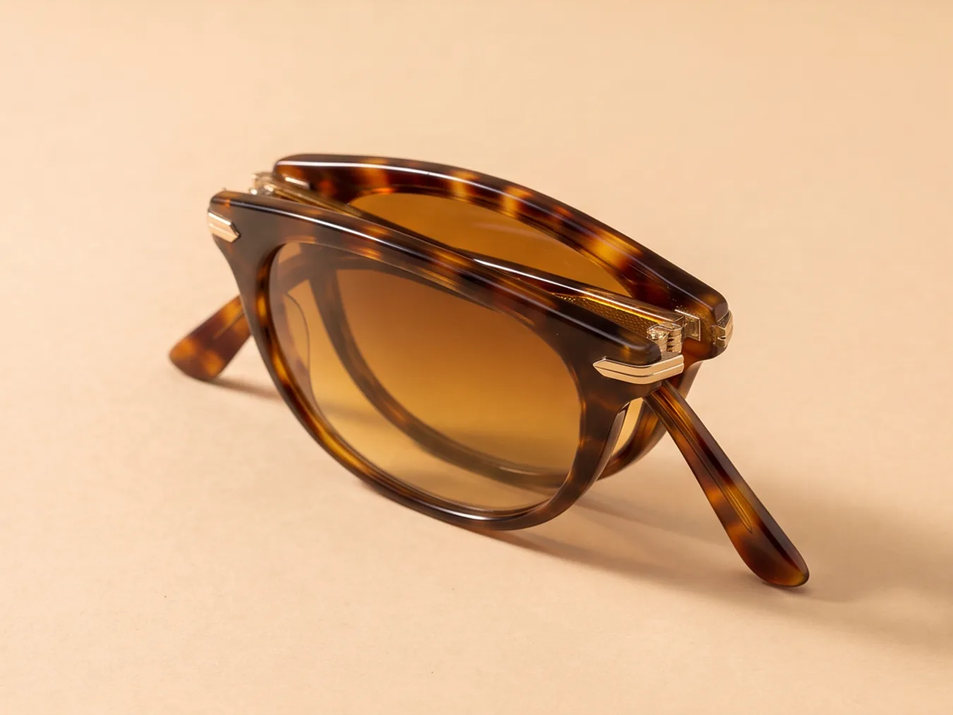 A pair of tortoiseshell sunglasses on a sand backdrop, from a new angle