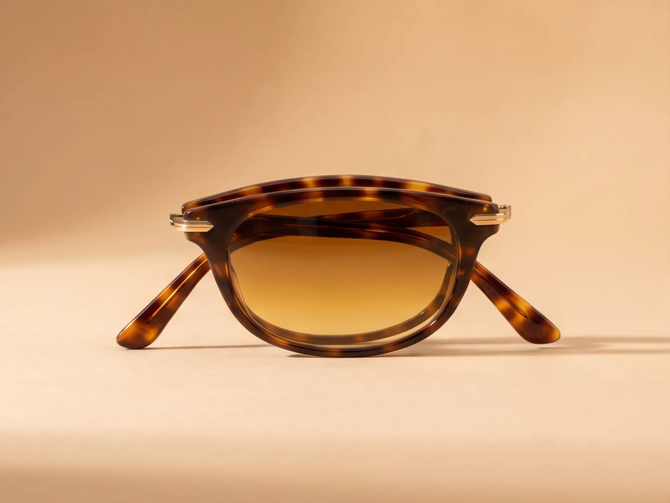 A pair of tortoiseshell sunglasses on a sand backdrop, from a new angle