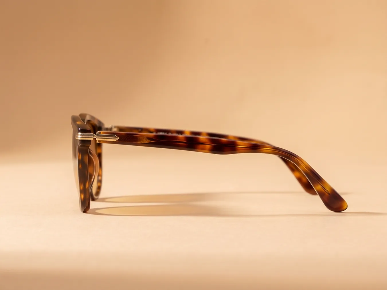 A pair of tortoiseshell sunglasses on a sand backdrop, from a new angle