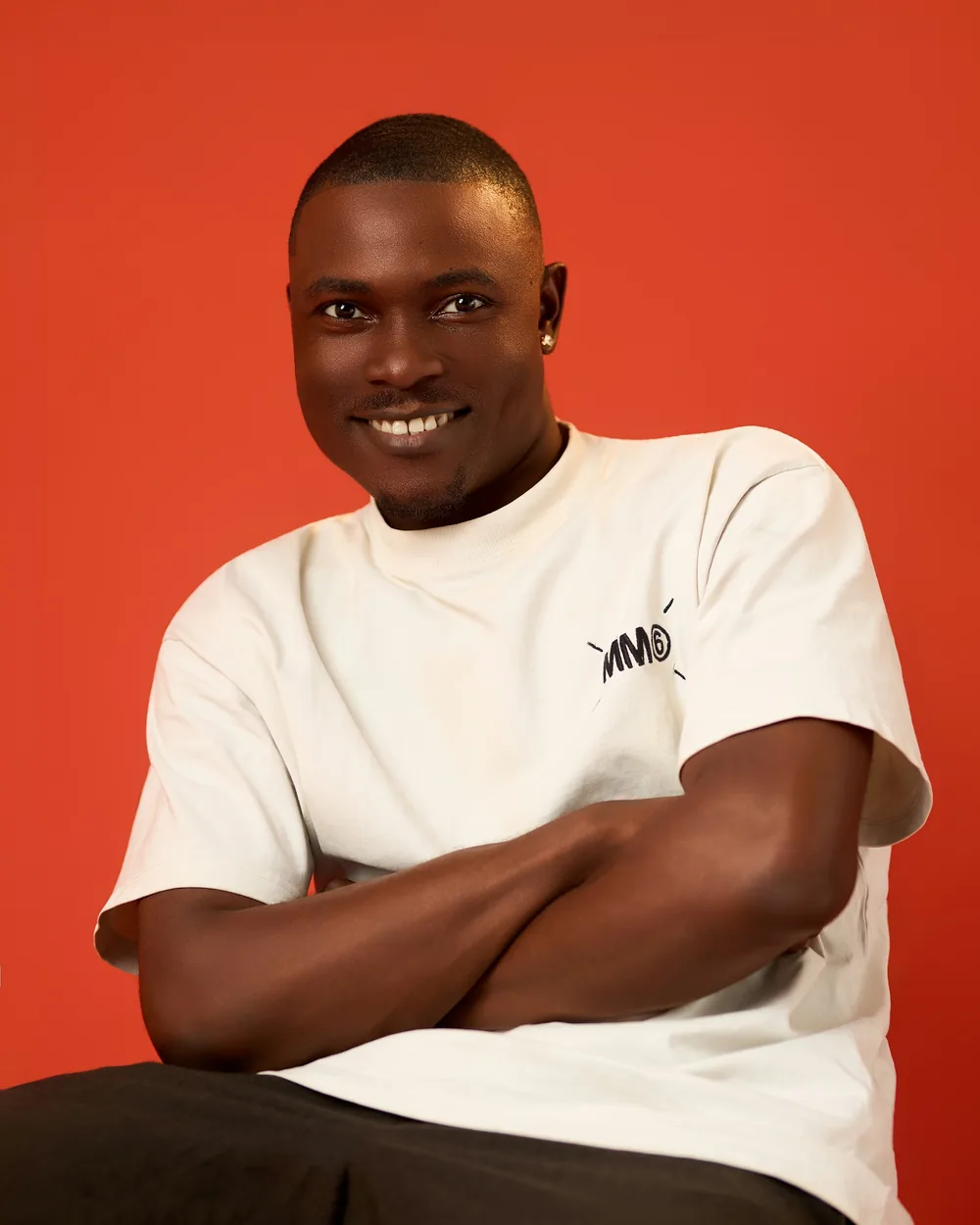 The same man seated, arms crossed, smiling