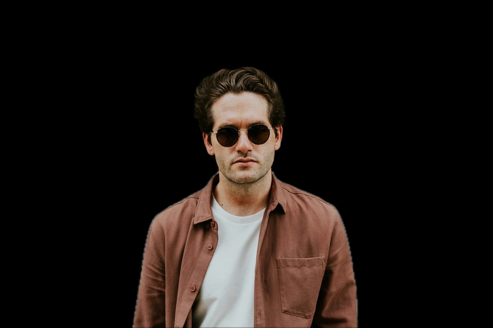 A man in sunglasses and a brown shirt against a brick wall, background removed