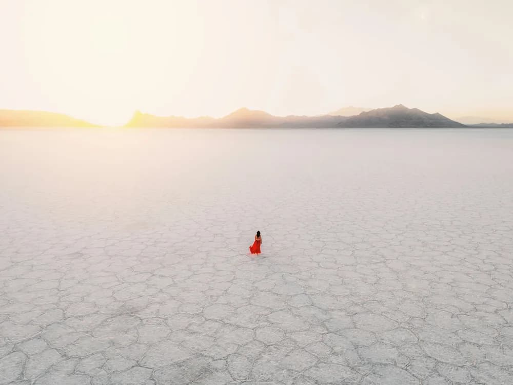A figure in red far out on a white salt flat at sunrise