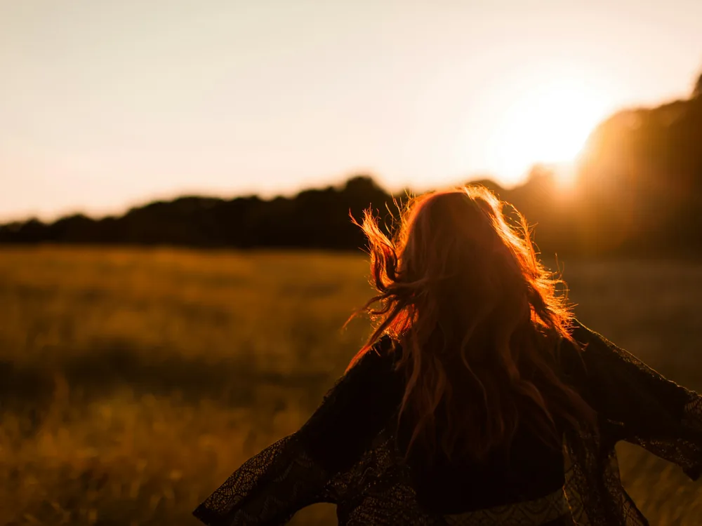 A woman walking into a field against the setting sun