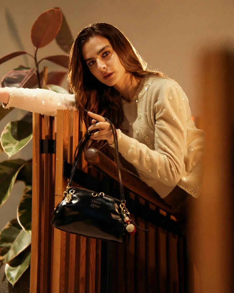 A black leather handbag held against a wooden rail