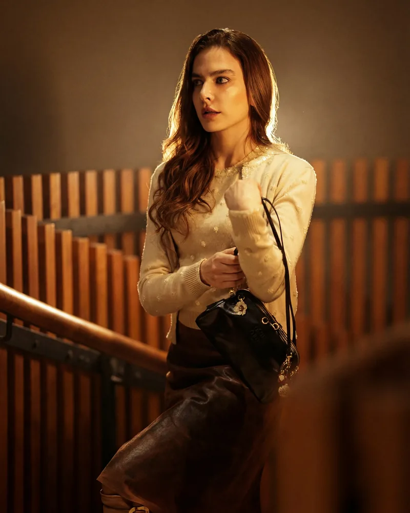 The same woman in a cream cardigan and brown leather skirt