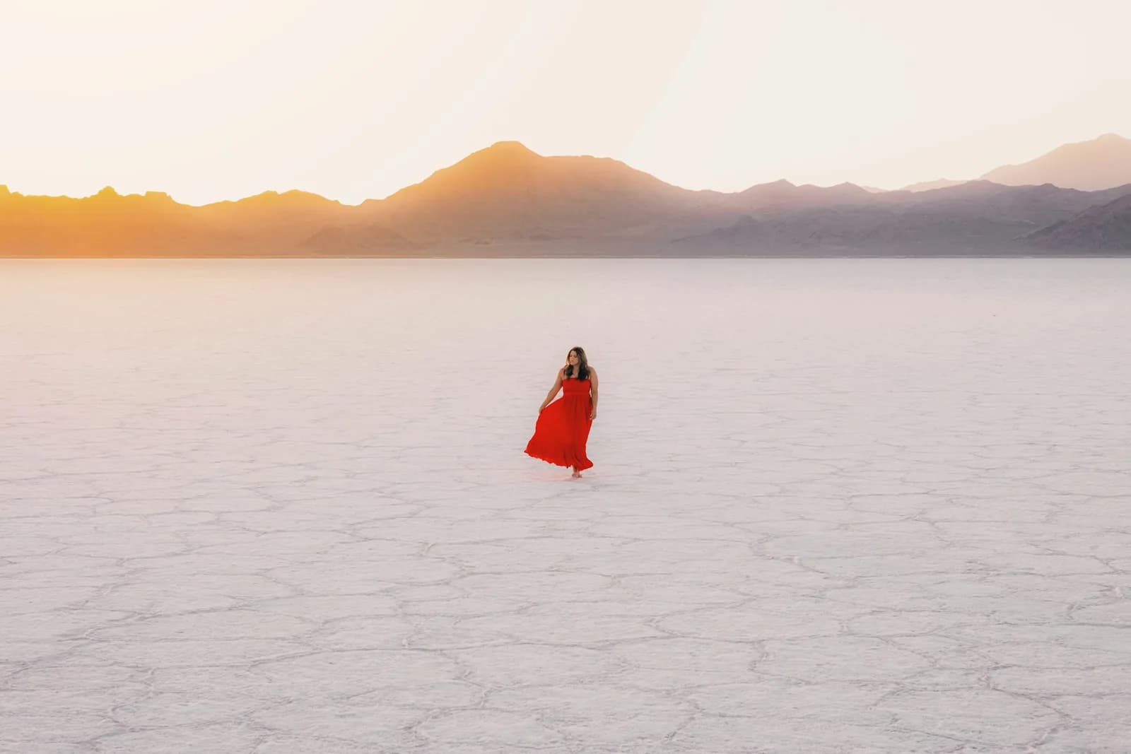 A woman in a red dress standing on a white salt flat below mountains
