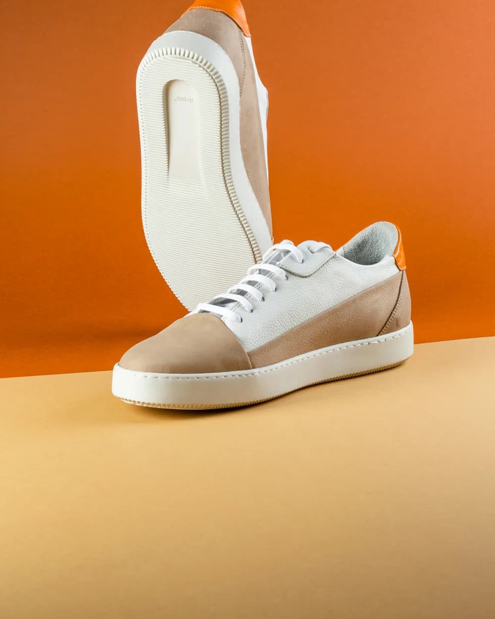 A suede and leather sneaker on an orange backdrop