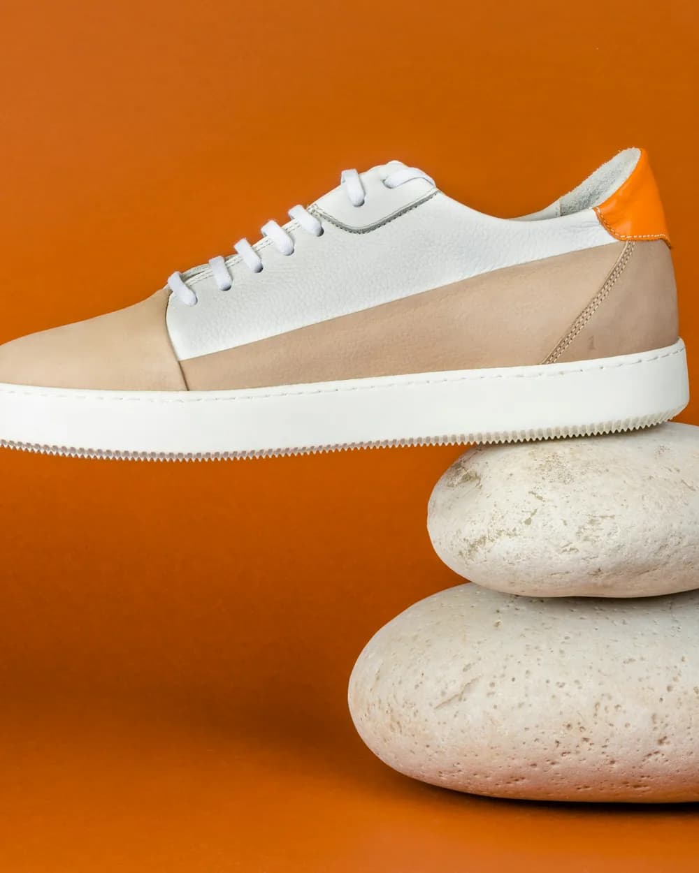 A sneaker balanced on two pale stones against orange