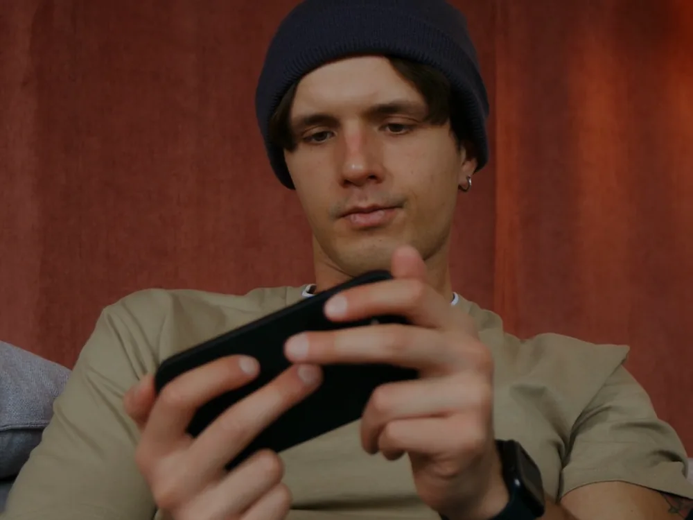 A man scrolling his phone against a red wall