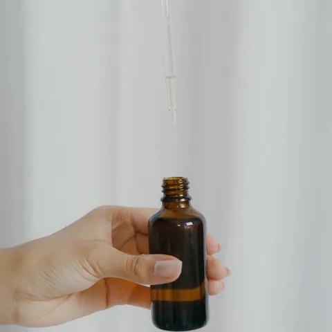 A hand holding a dropper bottle of oil