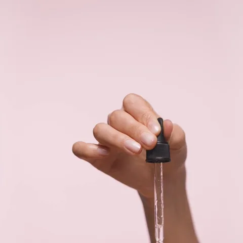 A dropper over an open palm against pink