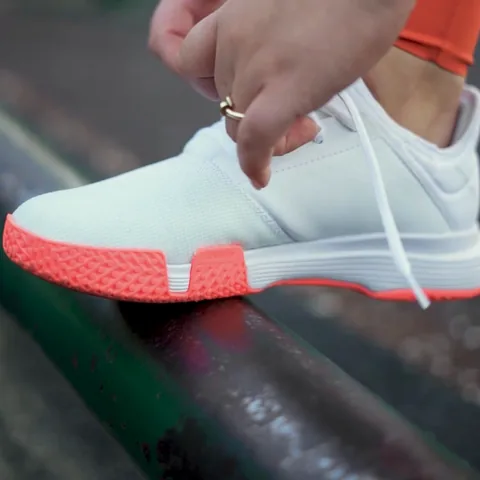 Hands tying a white and coral sneaker