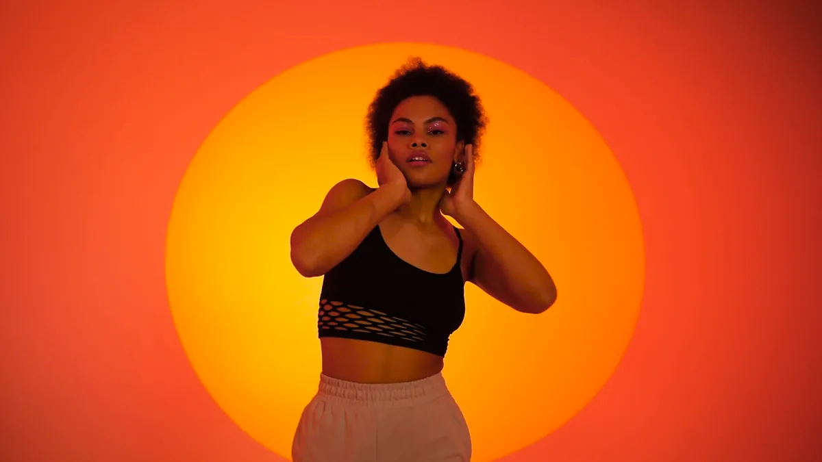 A dancer with her arms raised in front of an orange backdrop
