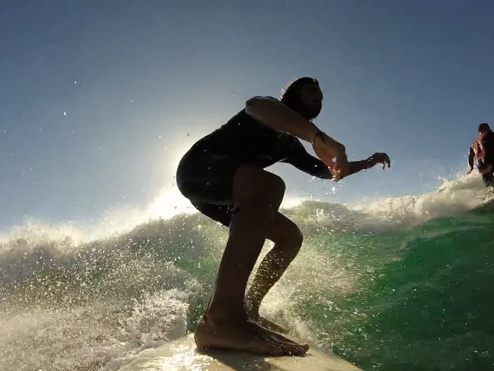 A surfer on a green wave against the sun