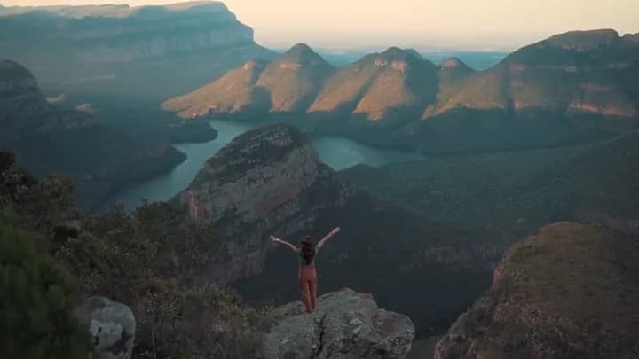 A woman with her arms open on a rock above the canyon