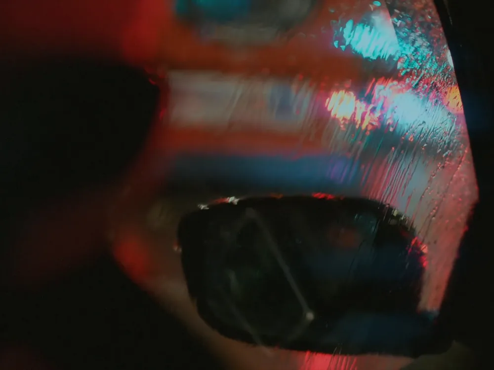 A car’s side mirror streaked with rain and neon