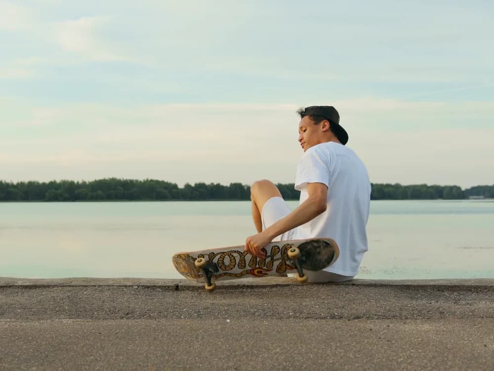 A skater sitting by a river with a skateboard