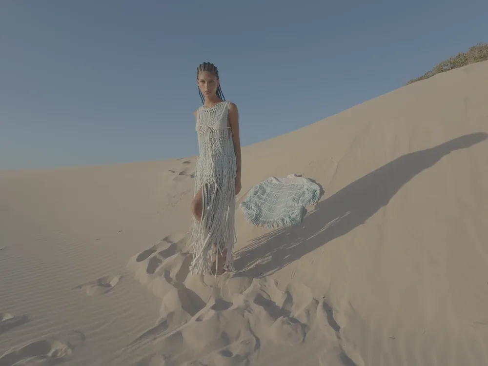 A woman in a pale fringed dress on a sand dune