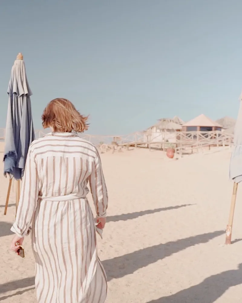 A woman in a striped shirt dress walking on sand