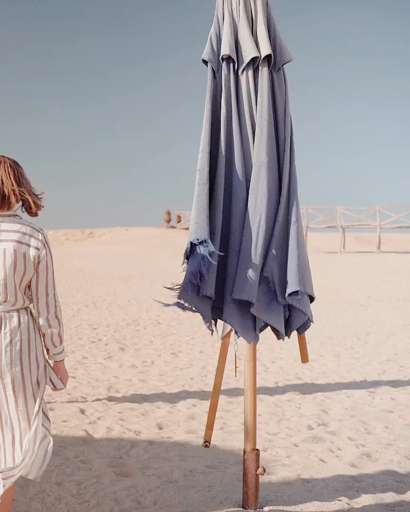 A closed navy beach umbrella on an empty beach